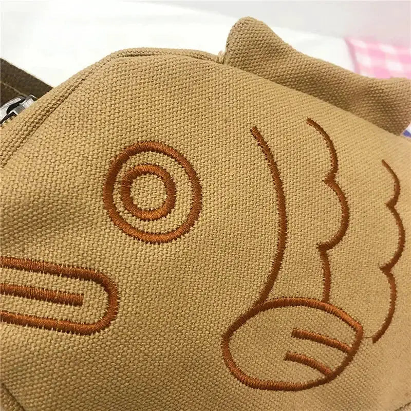 Fish-shaped brown canvas messenger bag with embroidered design and zipper pocket