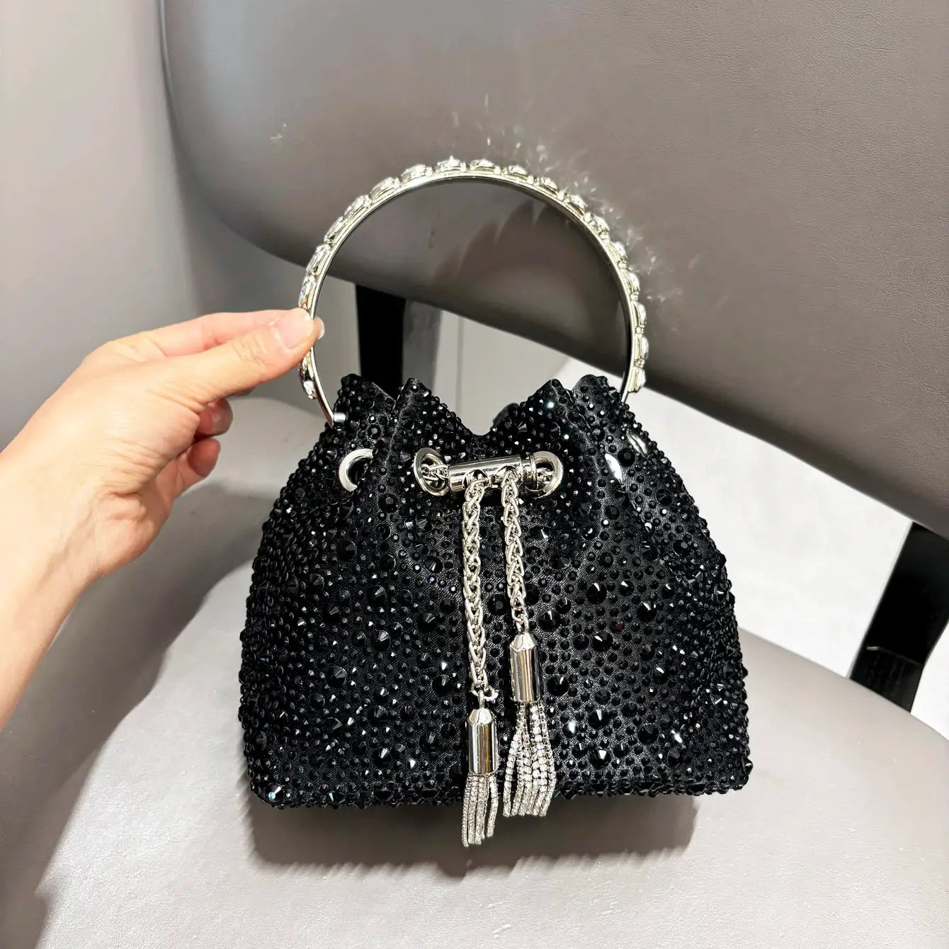 Black rhinestone bucket clutch with crystal-embellished round metal handle and tassel accents, evening bag