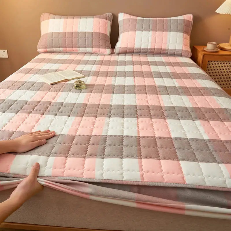 Quilted plaid mattress protector in pink, gray and white with matching pillows on a bed