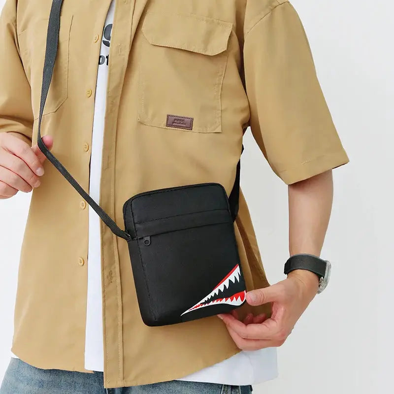 Crossbody bag, black, single-shoulder style with shark-teeth graphic and front zip pocket.