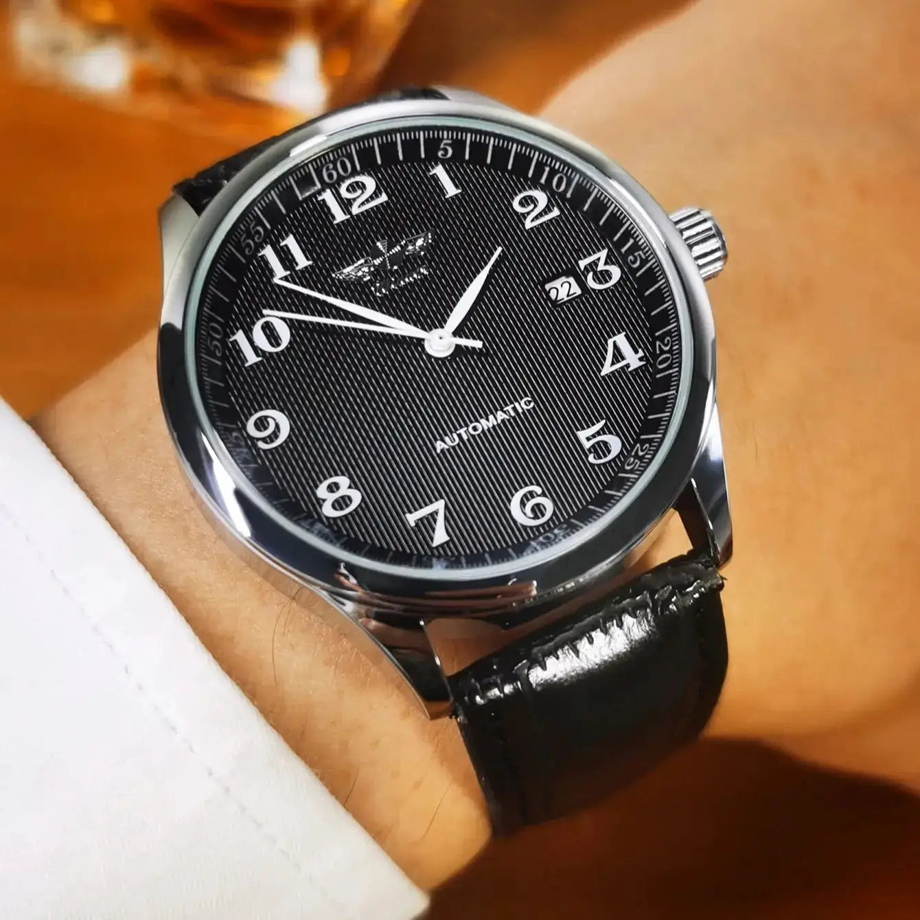Men's black dial wristwatch with leather strap, stainless steel case, white Arabic numerals, date window, automatic movement.