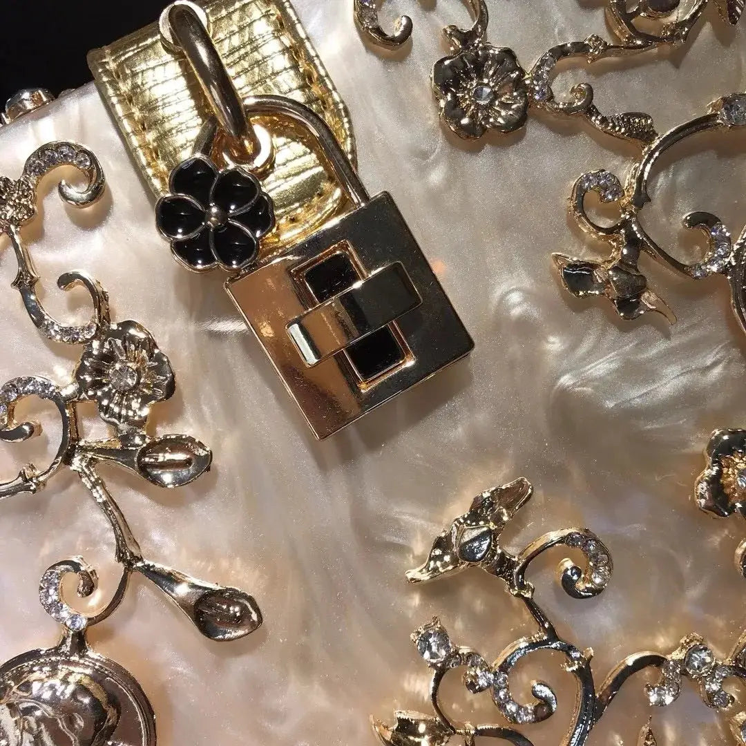 Gold-toned crystal evening bag with hollow metal box, black flower charm, and geometric clasp.