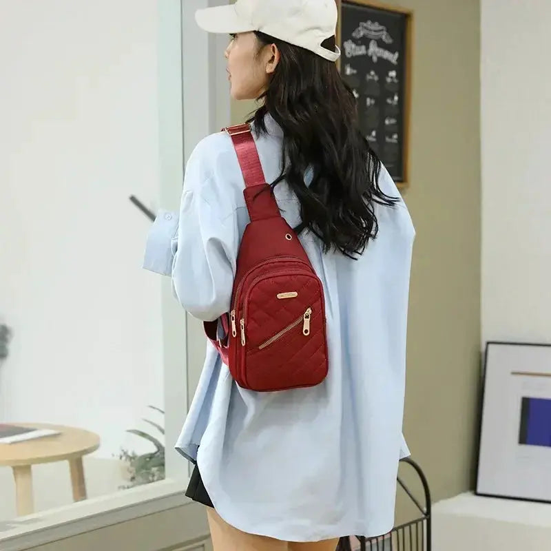 Red quilted mini backpack with gold zippers worn on the back by a woman in a light blue shirt