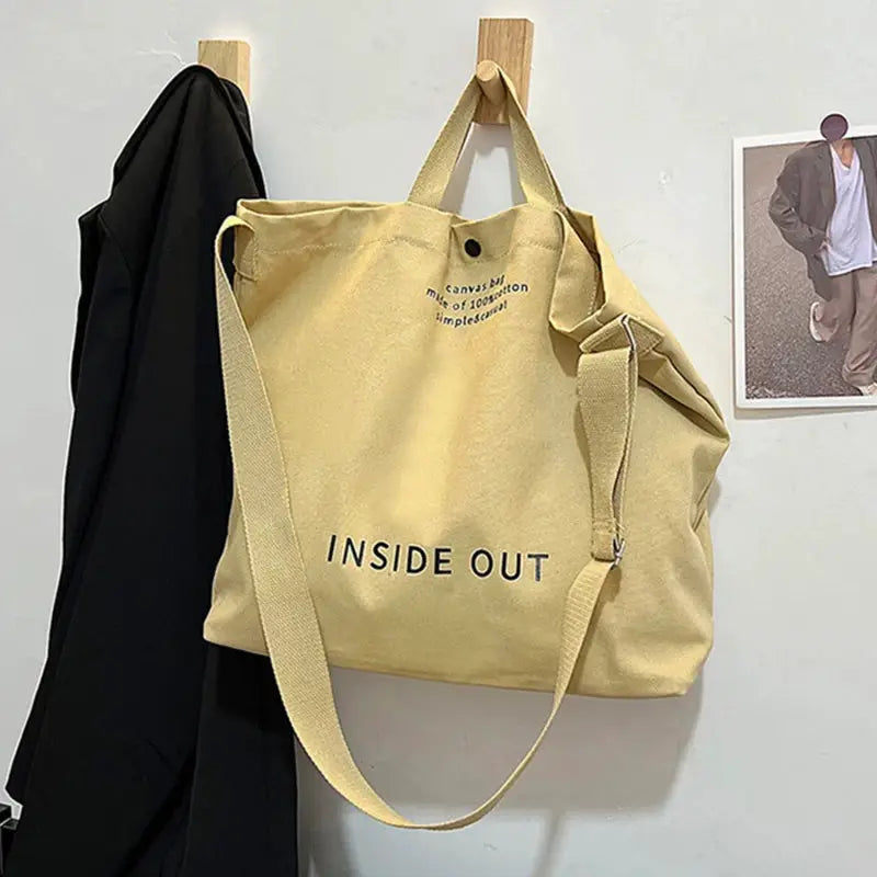 Beige canvas cross-body bag with long adjustable strap and INSIDE OUT print, large capacity.