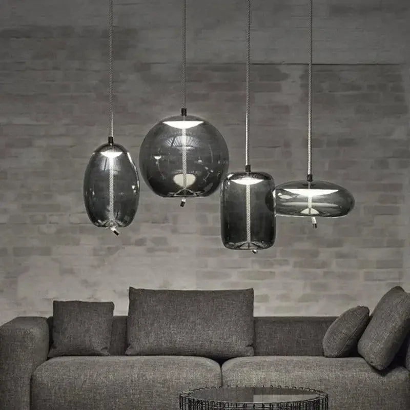 Four minimalist blue-tinted glass pendant lamps with hemp rope cords hanging over a gray sofa.