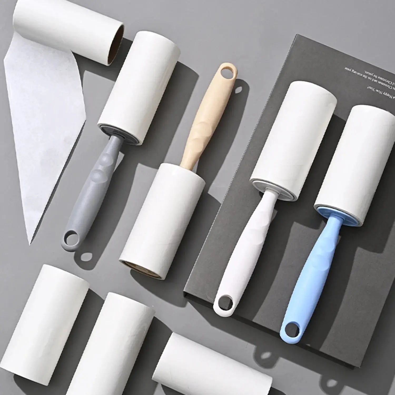Lint roller set by Simples Market with replaceable rolls and assorted handles in gray, beige wood, and blue