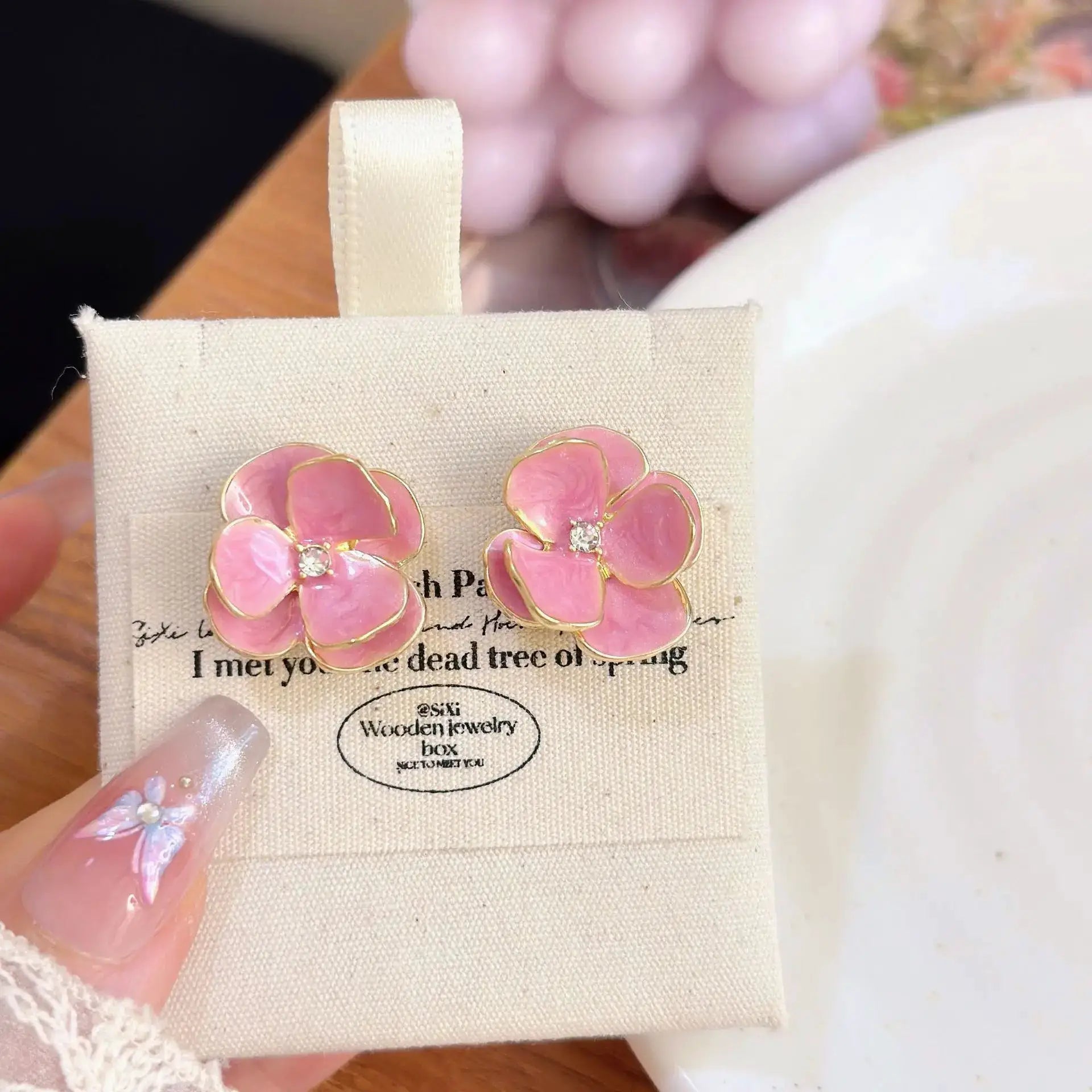 Pink enamel flower earrings with gold edging and crystal centers on a beige display card