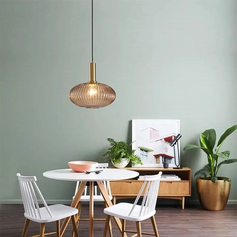 Nordic glass pendant light in cognac with brass cap, E27 hanging lamp over a white round dining table.