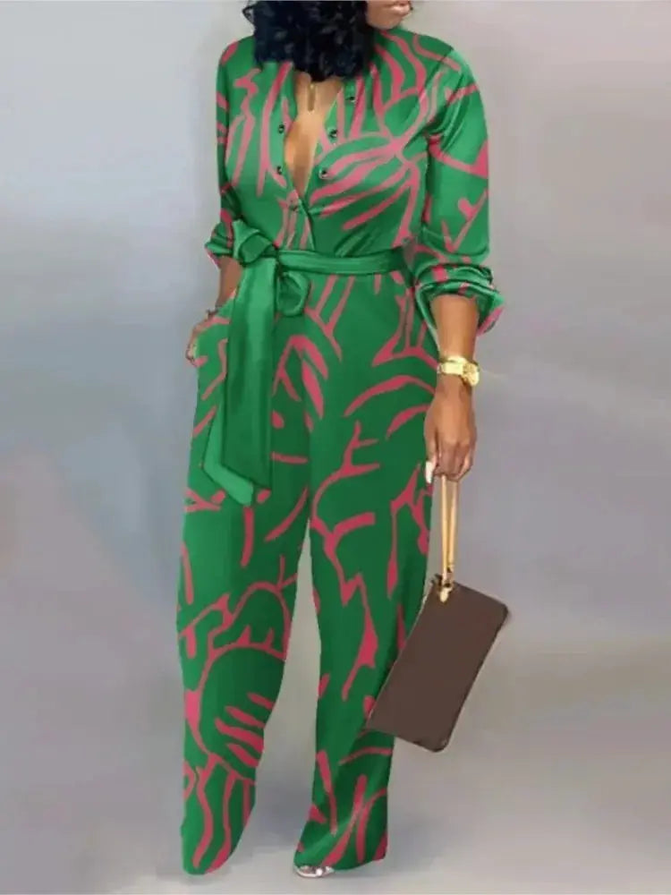 Green jumpsuit with pink abstract print, button-front V-neck, waist tie belt, long sleeves, wide-leg pants.
