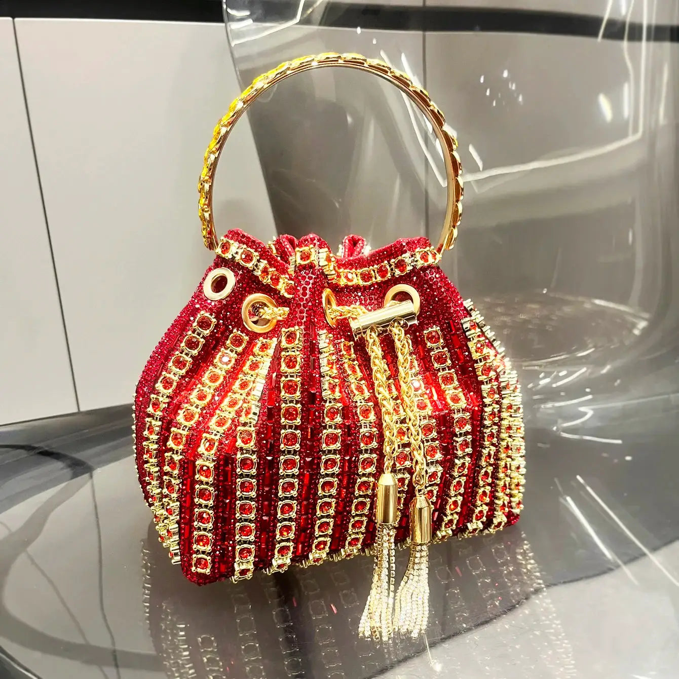 Red crystal-embellished bucket clutch with gold ring handle and tassel accents