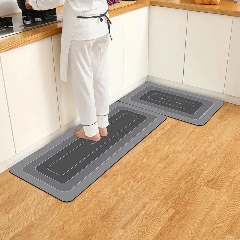 Two gray diatomite kitchen floor mats, waterproof and anti-slip, placed on a wooden kitchen floor.