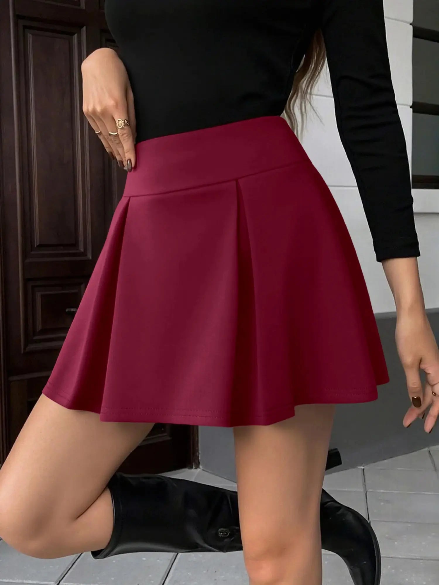 Mini skirt, red high-waist pleated A-line style, shown with black top.
