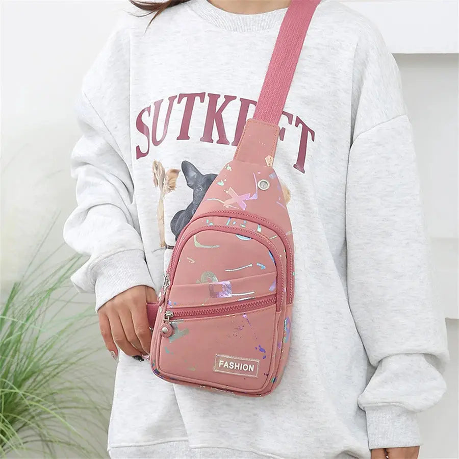 Chest bag crossbody sling backpack in pink with paint-splatter print and front zipper pocket.
