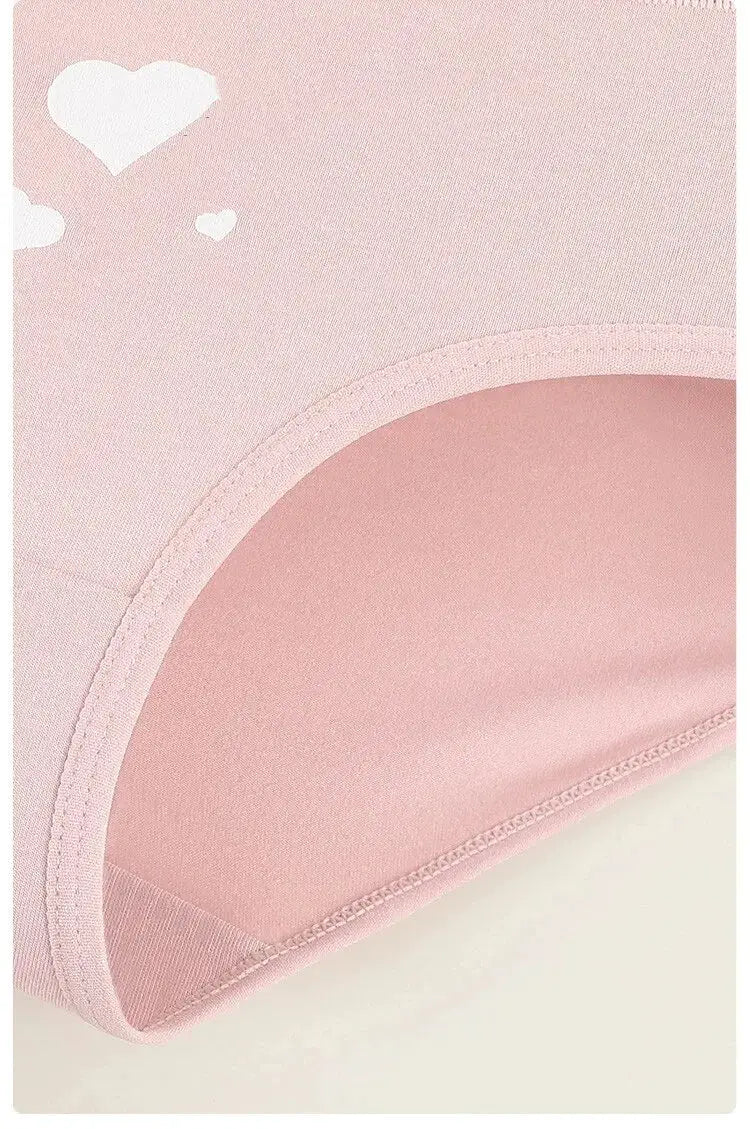 Pink women's cotton panties with white heart print, close-up fabric detail.