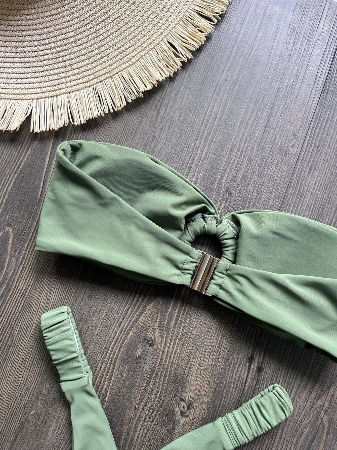 Olive green bikini set with metal back clasp top on a wooden surface beside a straw hat