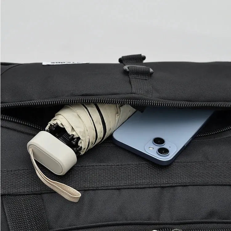 Oversized black handbag with a front pocket holding a folded umbrella and blue smartphone.