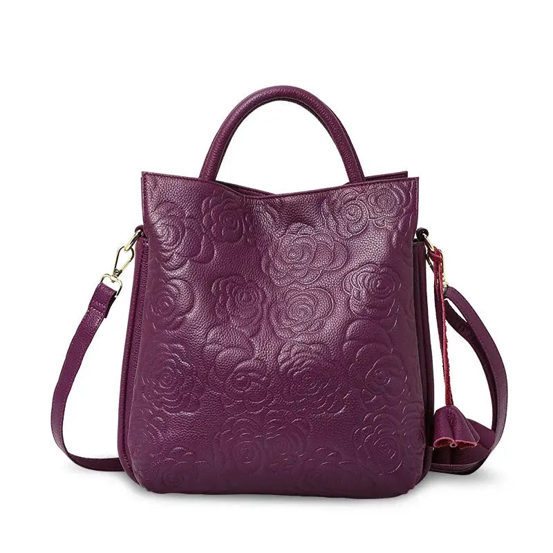 Purple cowhide handbag with embossed floral pattern, top handle and detachable shoulder strap.