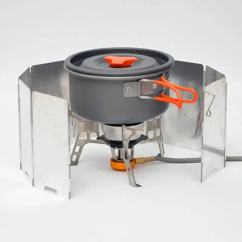 Gas stove with aluminum wind shield panels for camping, grey pot with orange knob.