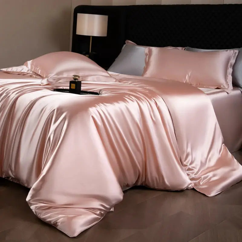Silk bed sheets set in blush pink with matching pillowcases on a bed.