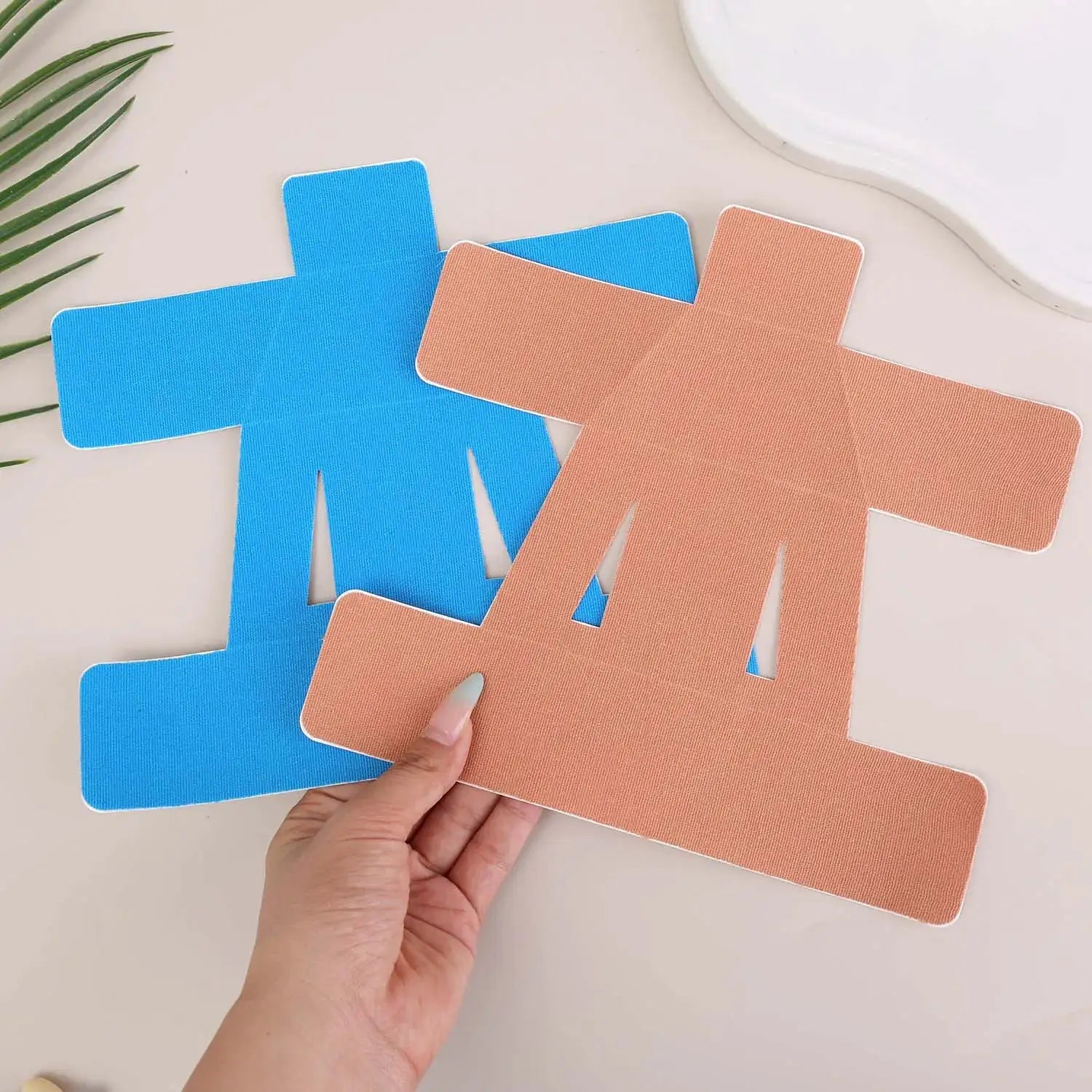 Shoulder kinesiology tape precuts in blue and peach, cross-shaped patches held in hand; several patches visible