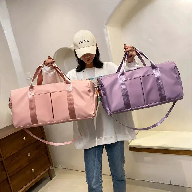 Two large fitness duffel bags in pink and lavender with top handles and shoulder straps held by a person