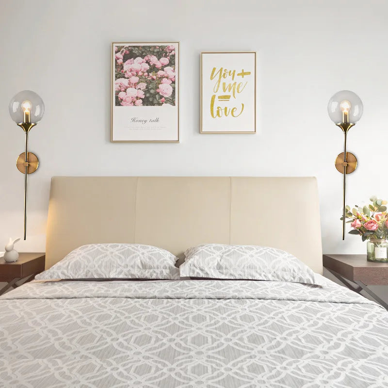 Simples Market modern glass ball wall lamp sconce pair with brass-gold finish and clear glass globes beside a bed.