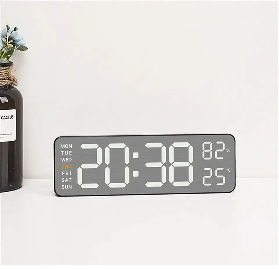 Digital wall clock with mirror-brushed finish; large LED time display, left weekday list, right 82% humidity and 25°C.