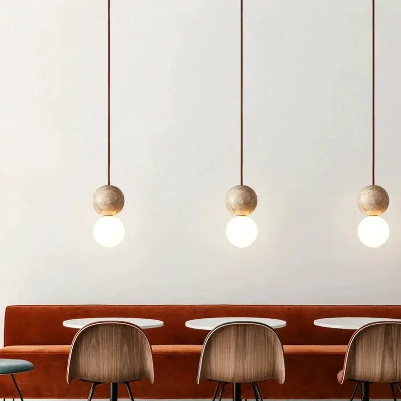 LED pendant light trio with stone cream wooden spheres and globe bulbs over a dining banquette