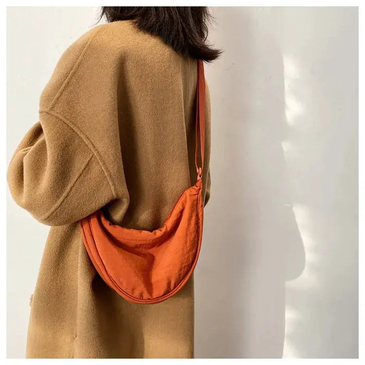 Casual nylon hobo crossbody bag in orange with a long strap, shown worn over a camel coat.