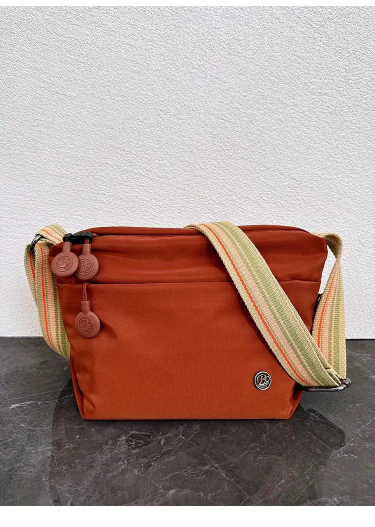 Ultra-light rust-orange nylon crossbody bag with an adjustable wide striped strap and zipper closure.