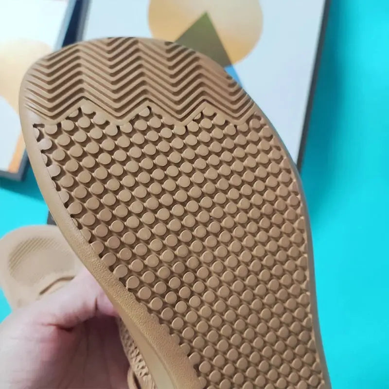 Men's wide-toe minimalist sports shoe outsole in tan rubber with circular grip studs and chevron tread.
