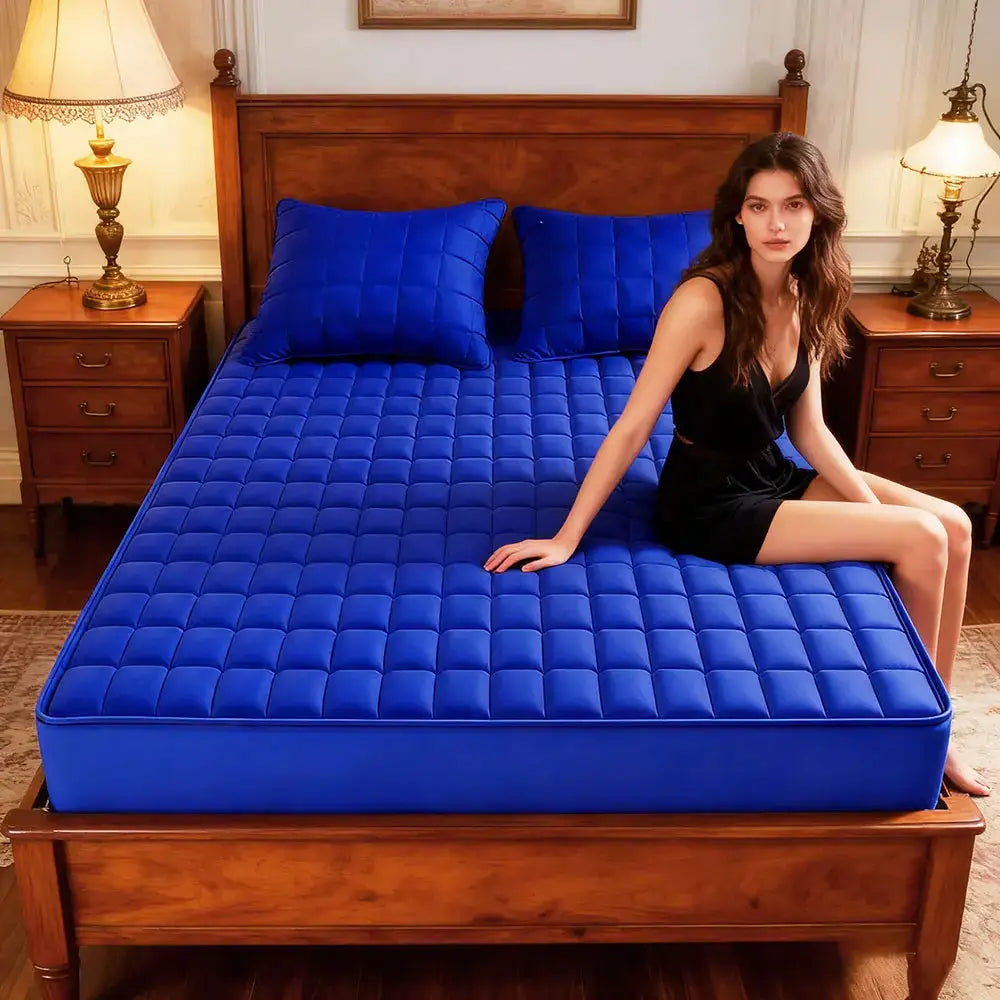 Blue quilted mattress protector pad on a wooden bed with two matching blue pillows