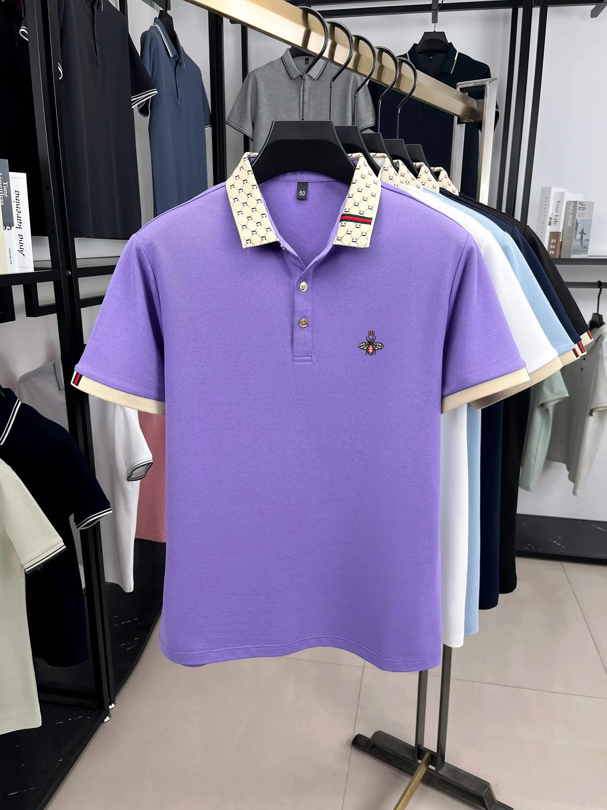 Polo shirt lavender with beige patterned collar and bee embroidery; five similar polos on display.
