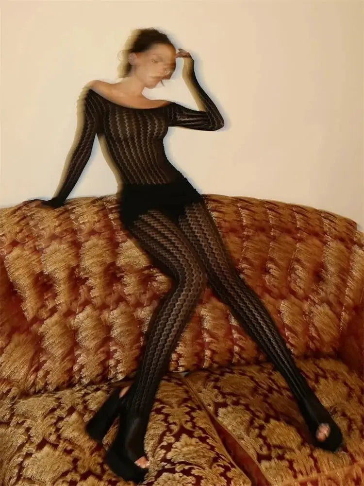 Tossy see-through black jumpsuit with mesh pattern, model seated on a patterned couch.