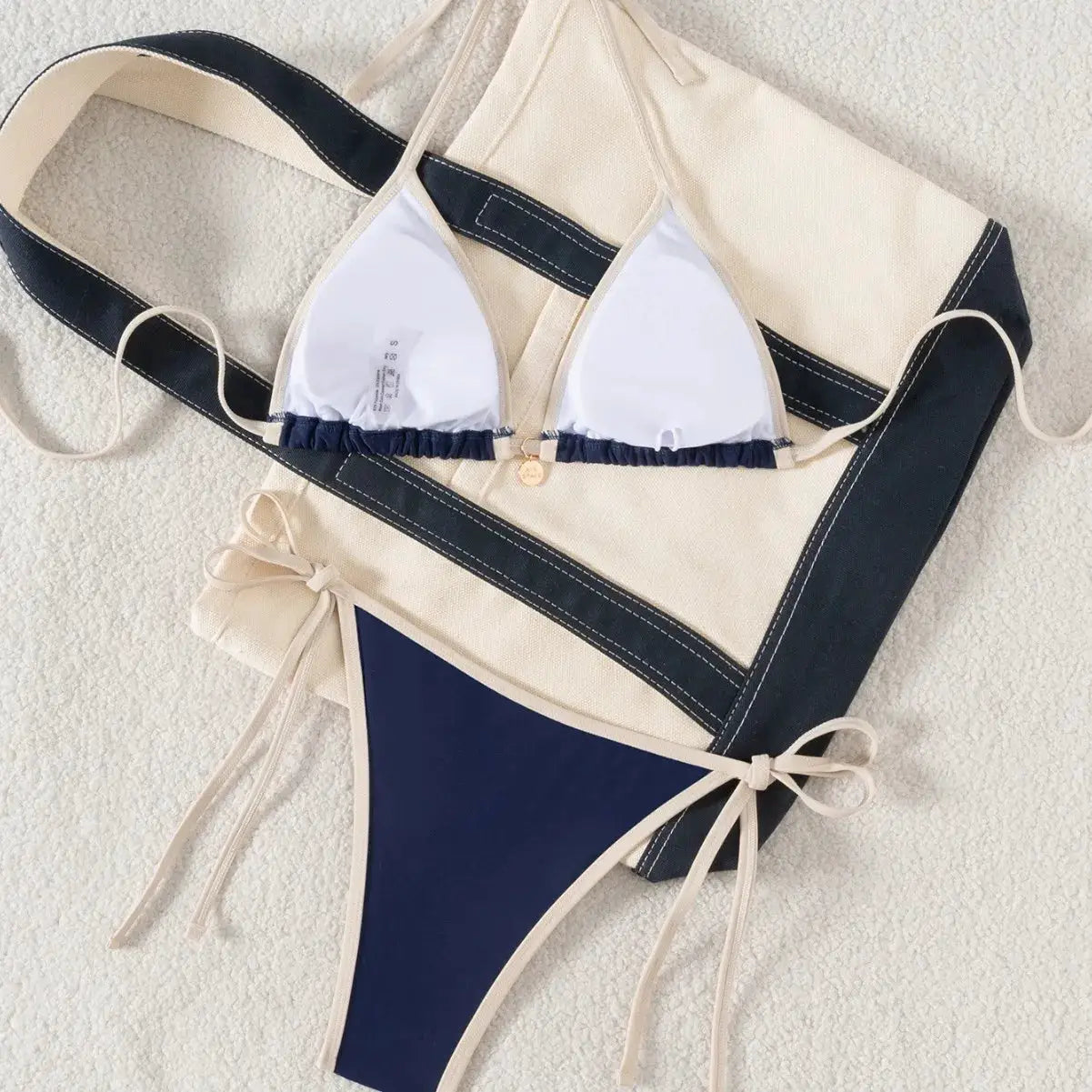 Two-piece bikini swimsuit with navy and beige color blocking; white triangle top with beige trim and edge-tie bottoms.