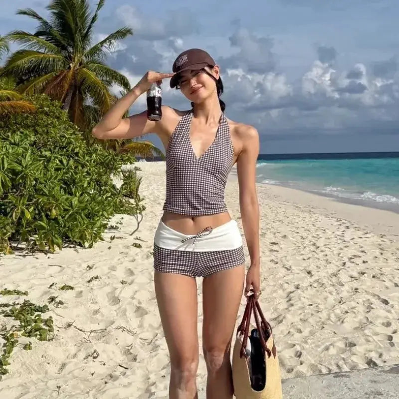 Two-piece bikini set with deep-V halter top and high-waisted black-and-white checkered bottoms on the beach.