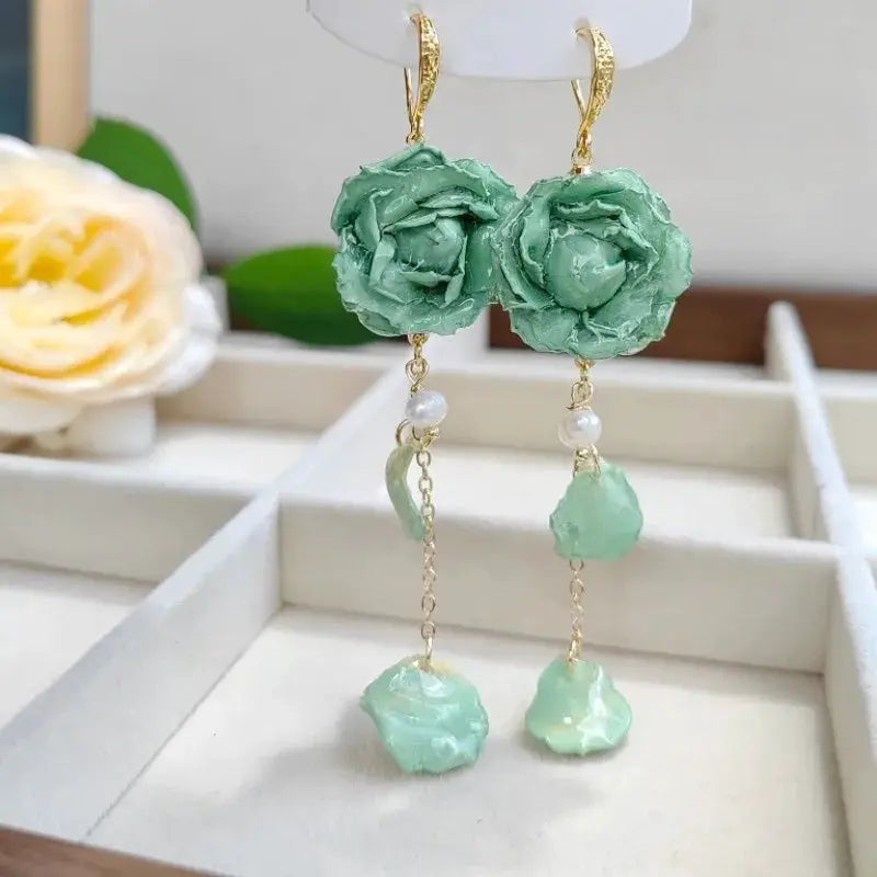 Pair of teal epoxy rose long earrings with gold hooks, pearl beads, and dangling green resin charms