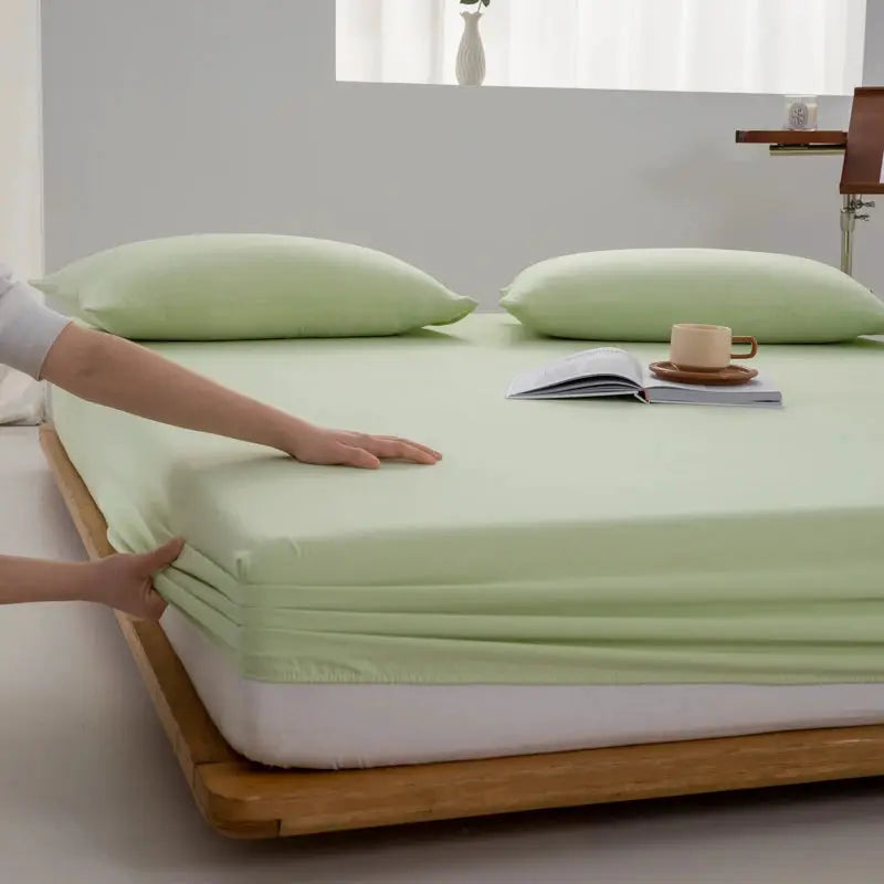 Soft cotton fitted sheet in mint green with elastic edges on a bed.