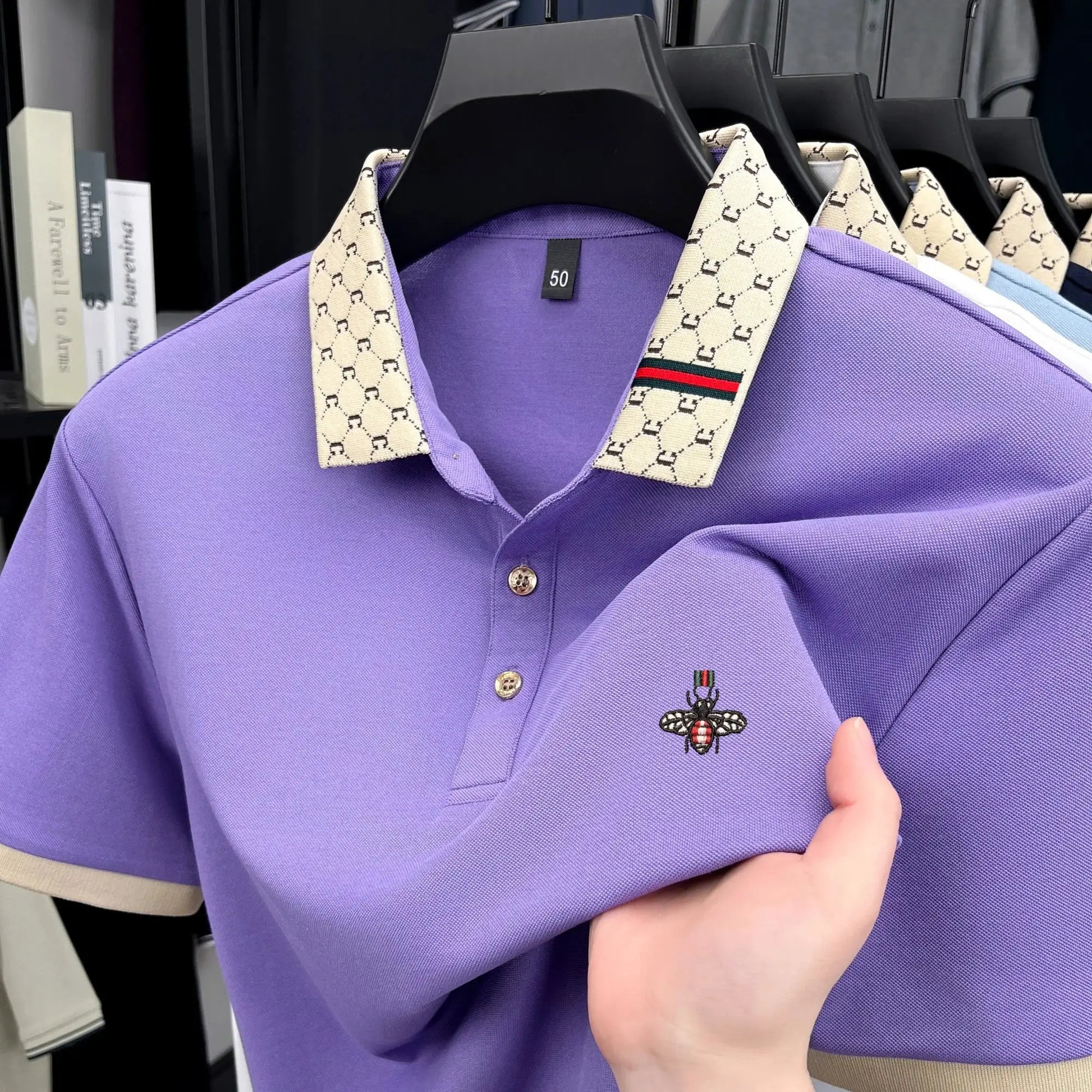 Men's purple polo shirt with beige logo-pattern collar, short sleeves, and bee embroidery.
