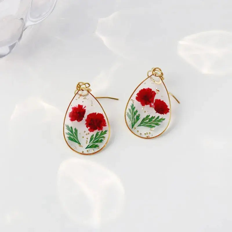 Pair of teardrop epoxy resin earrings with pressed red flowers and green leaves in a gold frame