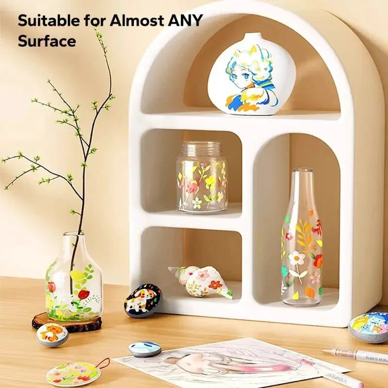 Decorative white arched display shelf with floral-painted glass bottles and shells on a wooden surface