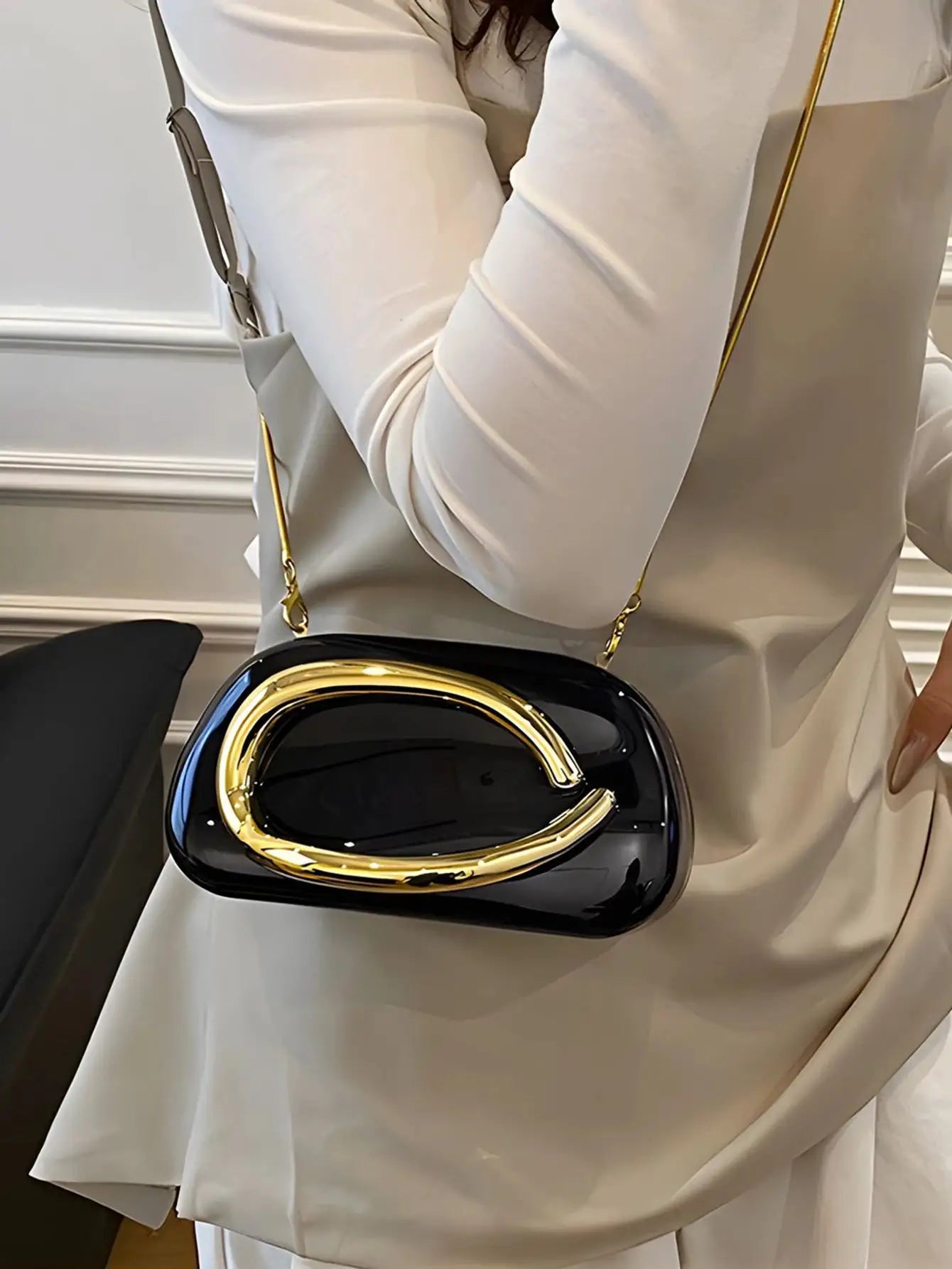 Acrylic box-shaped crossbody bag in glossy black with a gold-tone curved handle and strap