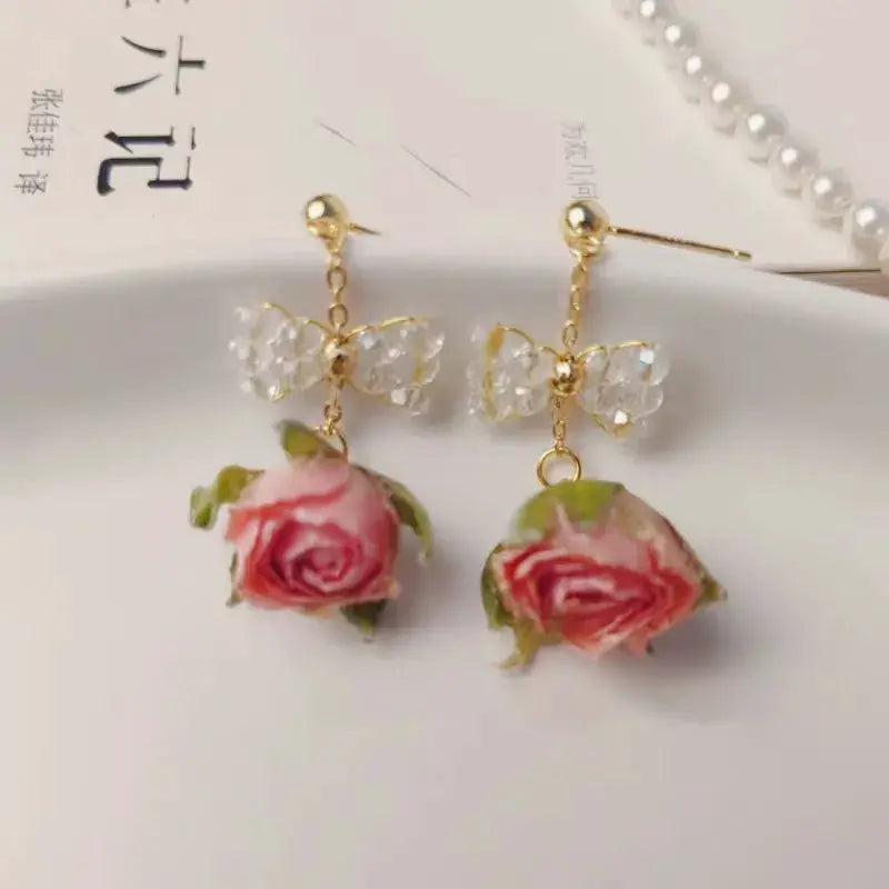 Red rose epoxy resin drop earrings by Simples Market with gold-tone posts and crystal bow accents