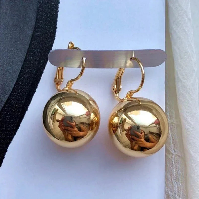 Pair of gold-tone ball drop earrings with smooth spherical pendants by Simples Market
