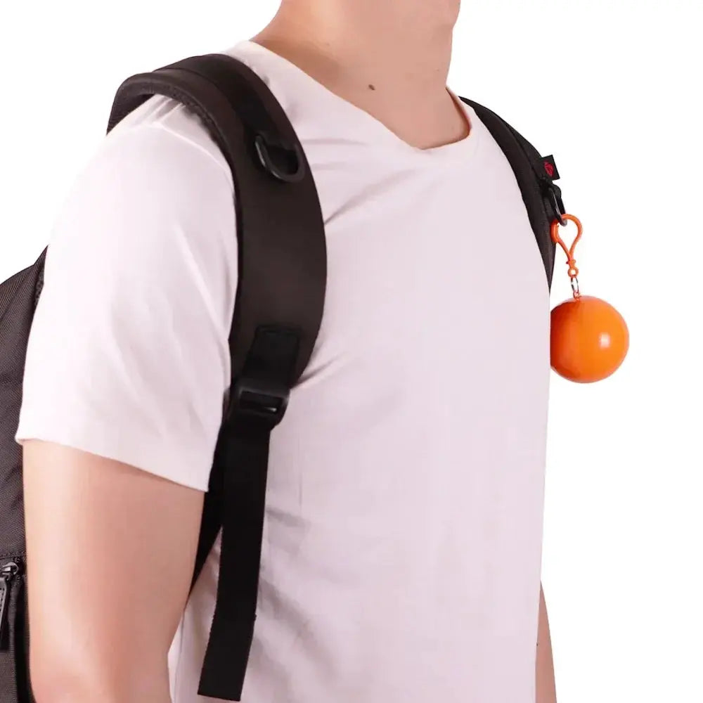 Orange pocket ball keychain for portable raincoat clipped to a backpack strap on a white-shirted traveler