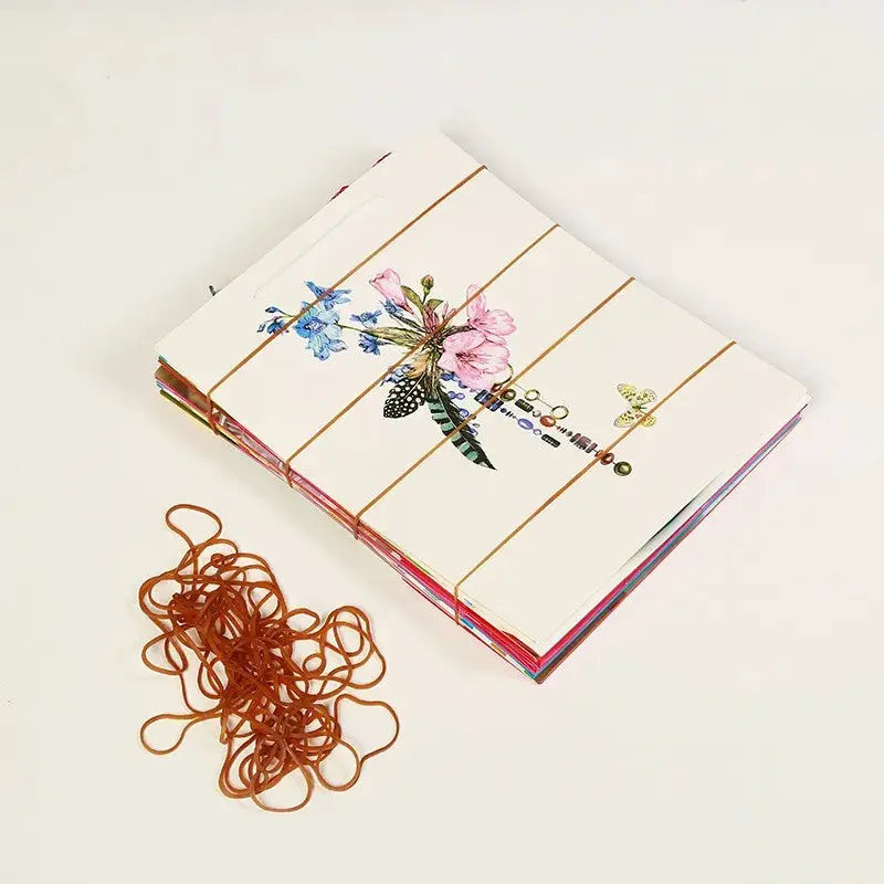 Rubber bands, yellow, 102×1.4mm, 50/100 pcs, shown with a stack of floral notebooks