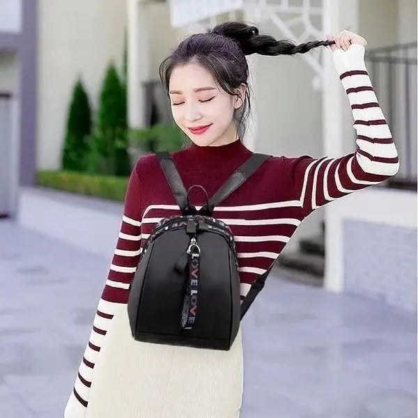 Women's black backpack with LOVE strap detail, worn by a model in a burgundy striped sweater.