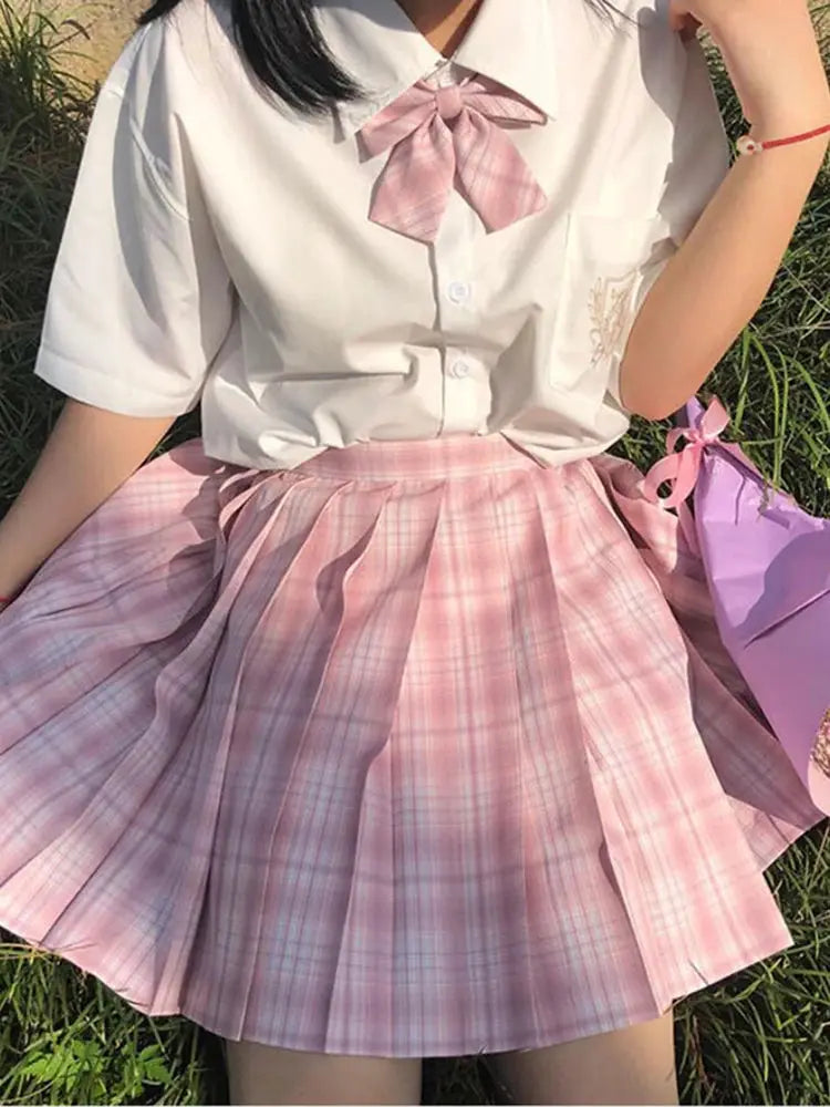 ZOKI pink plaid pleated high-waist mini skirt worn with white blouse and pink bow.