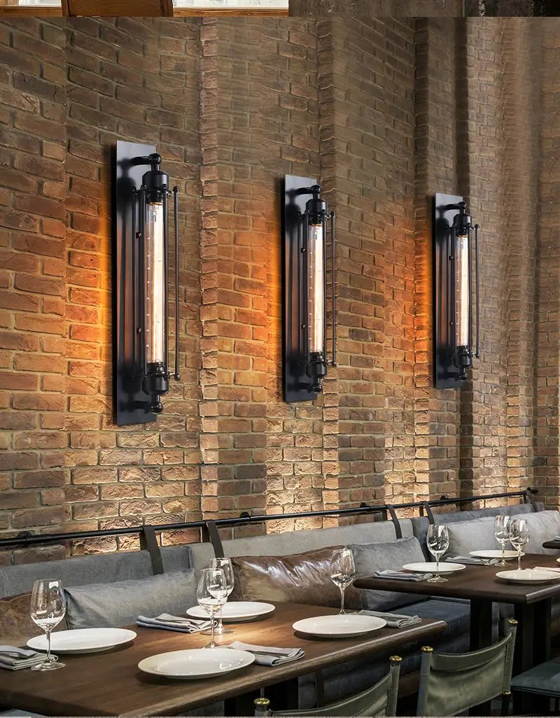Three retro industrial iron wall lights with black frames and Edison tubes on a brick wall above a dining table.