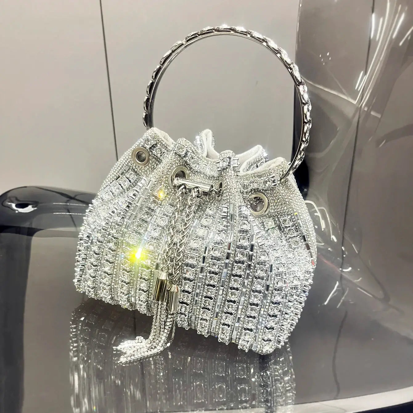 Simples Market crystal-embellished bucket clutch in silver with rhinestone strands and round metal handle